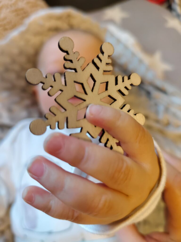Bild, in welchem ein Baby eine Holzschneeflocke in der Hand hält